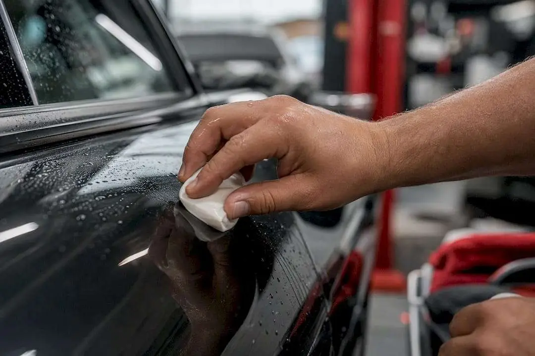 Hands using clay bar on car panel after adhesive removal