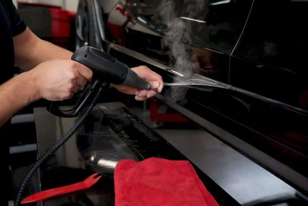 Hands steaming edge of paint protection film on car