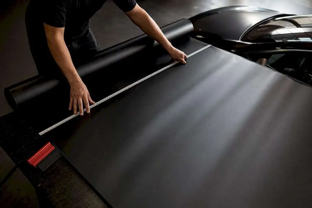 Hands measuring black vinyl over anonymous roof panel